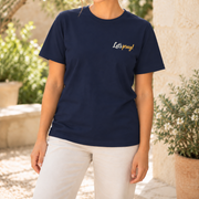Woman wearing the navy Pray One Hail Mary With Me T-Shirt with an ivory and gold Let's pray! chest print in a garden.