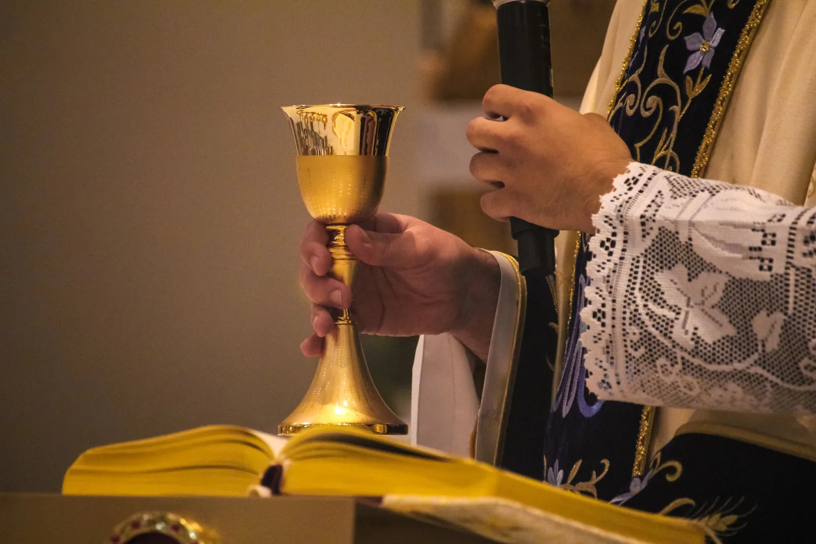 Hands holding a gold chalice above an open book at the altar.