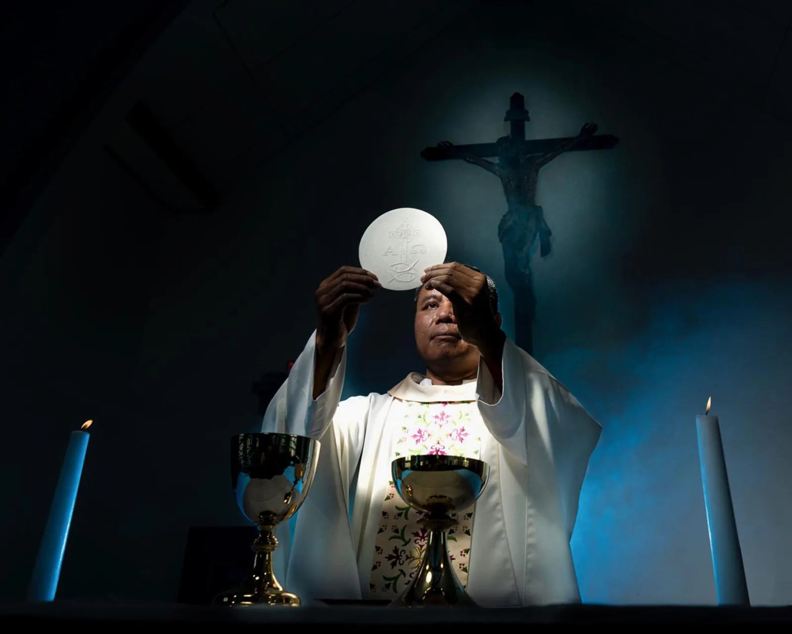 A priest lifting the round white host above the chalice.