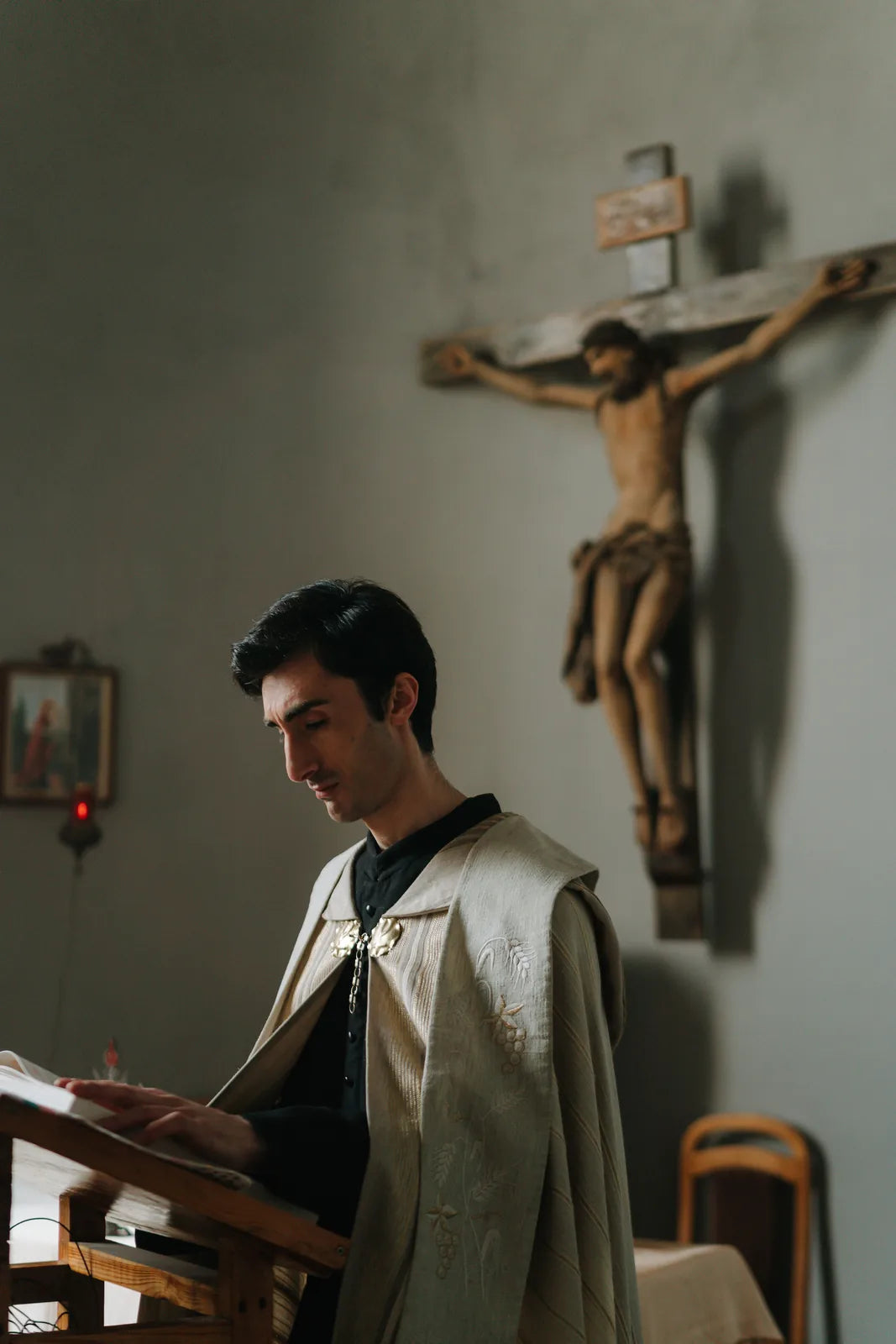 A young priest reading at a lectern beneath a crucifix.