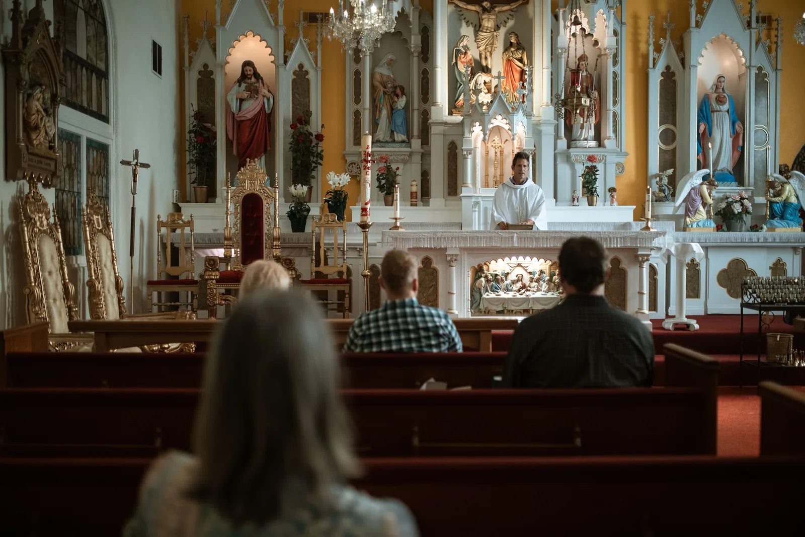 People in the pews of a church during Mass, the priest at a white altar.