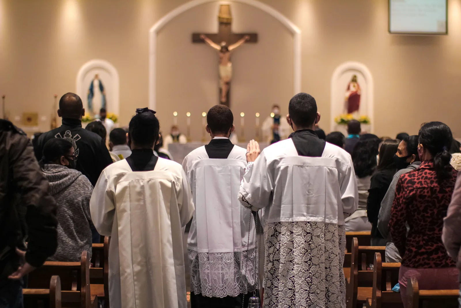 A congregation standing with altar servers in white, a crucifix above the altar.